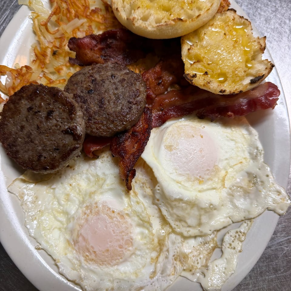 Hearty breakfast platter with fried eggs, bacon, sausage, hash browns, and buttered toast on a white plate.