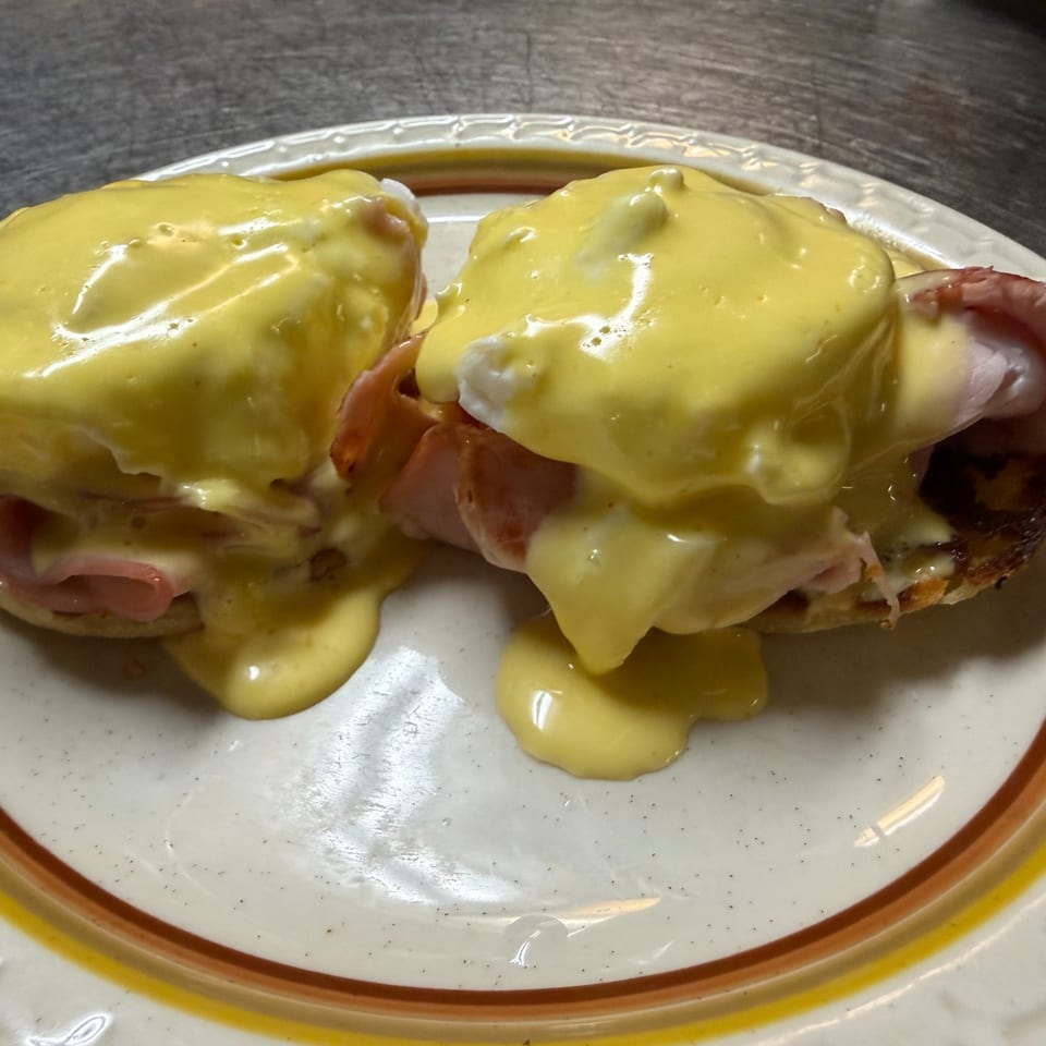 Two eggs Benedict with ham and poached eggs covered in hollandaise sauce on a decorative plate.