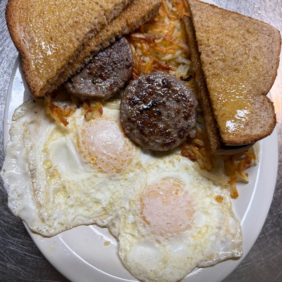Plate of grilled burger patties, toast, shredded potatoes, and two fried eggs.