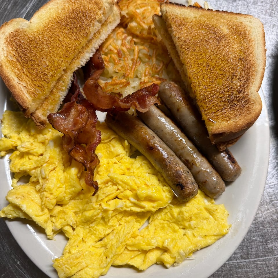 Breakfast platter with scrambled eggs, bacon, sausage links, hash browns, and buttered toast on a white plate.