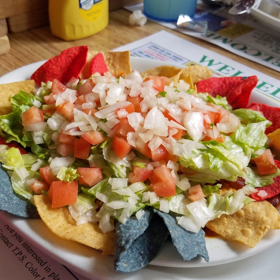 A plate of nachos with lettuce, diced tomatoes, and onions, surrounded by colorful tortilla chips.